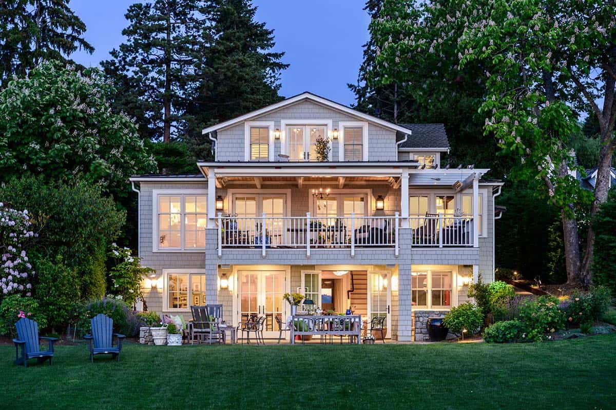 Twilight view of the home glowing with interior light, lawn chairs, and dining terrace