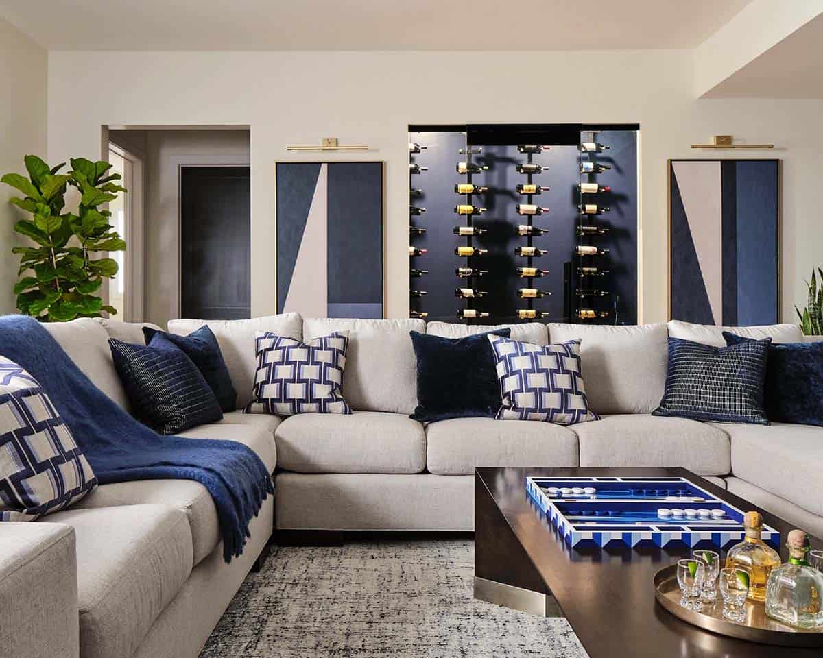 Close-up of beige sectional sofa with navy velvet and patterned pillows, backlit glass wine rack in background