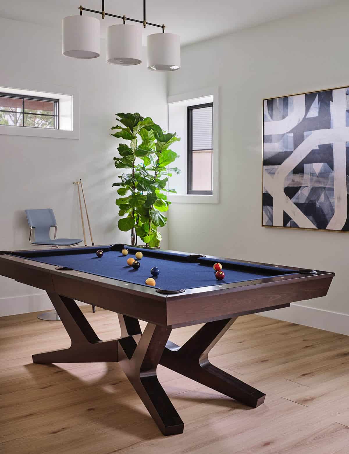 Game room with billiards table topped with blue felt, fiddle leaf fig plant, and abstract black-and-white artwork