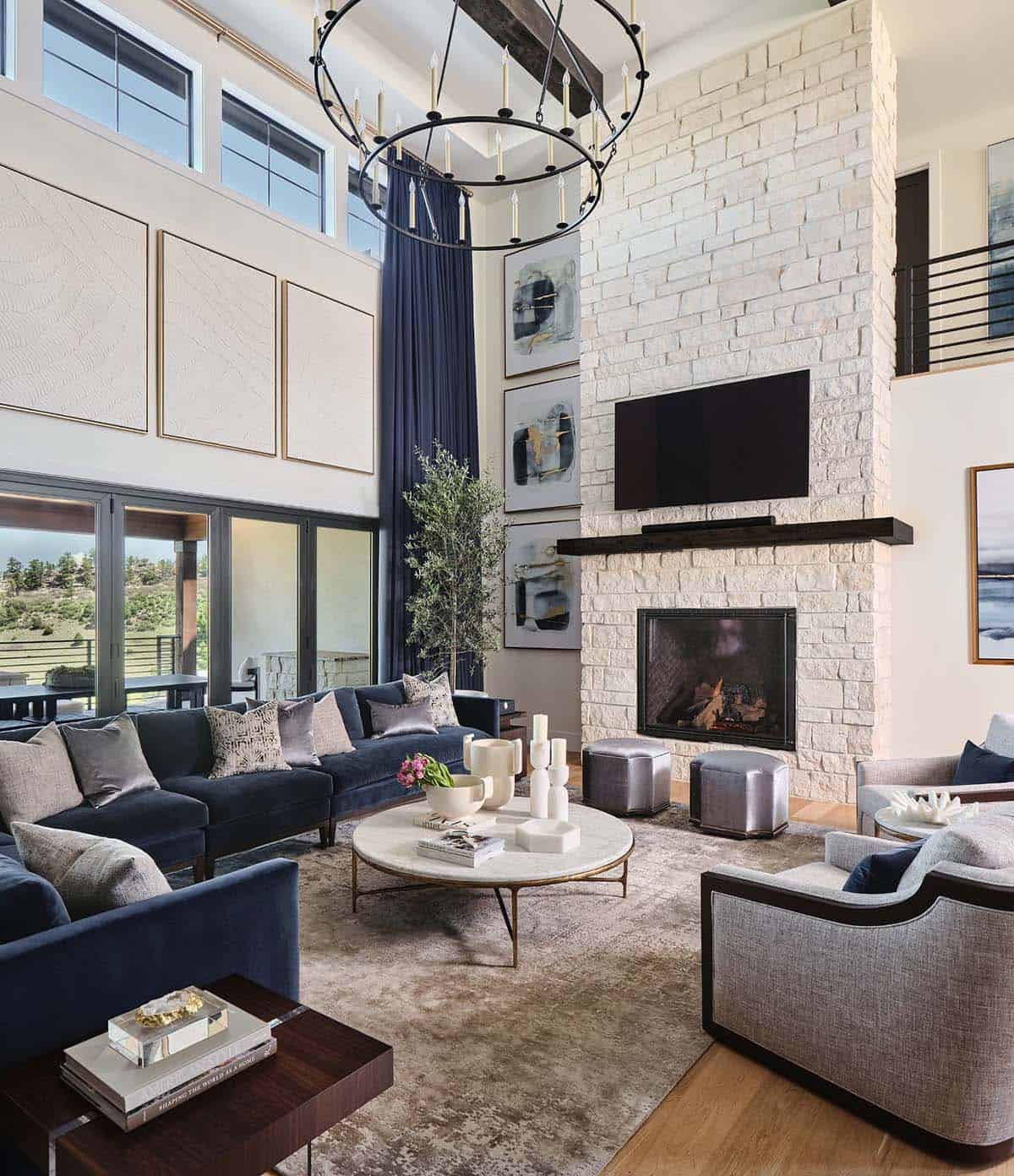 Living room with stone fireplace, mounted TV, navy sofas, round marble coffee table, and wrought iron chandelier