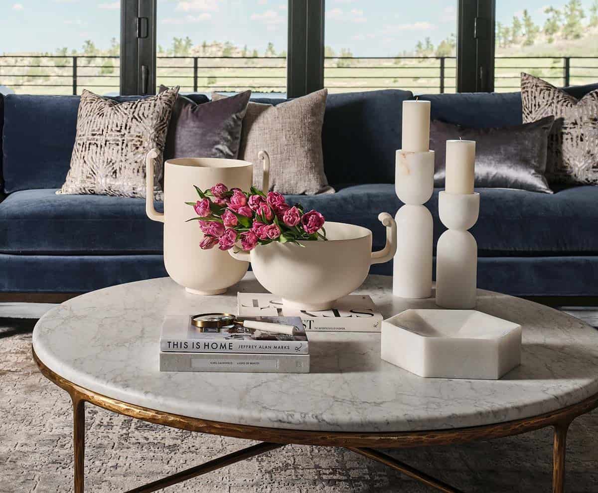 Coffee table vignette with cream ceramic vases, pink tulips, marble candlesticks, and navy velvet sofa in background