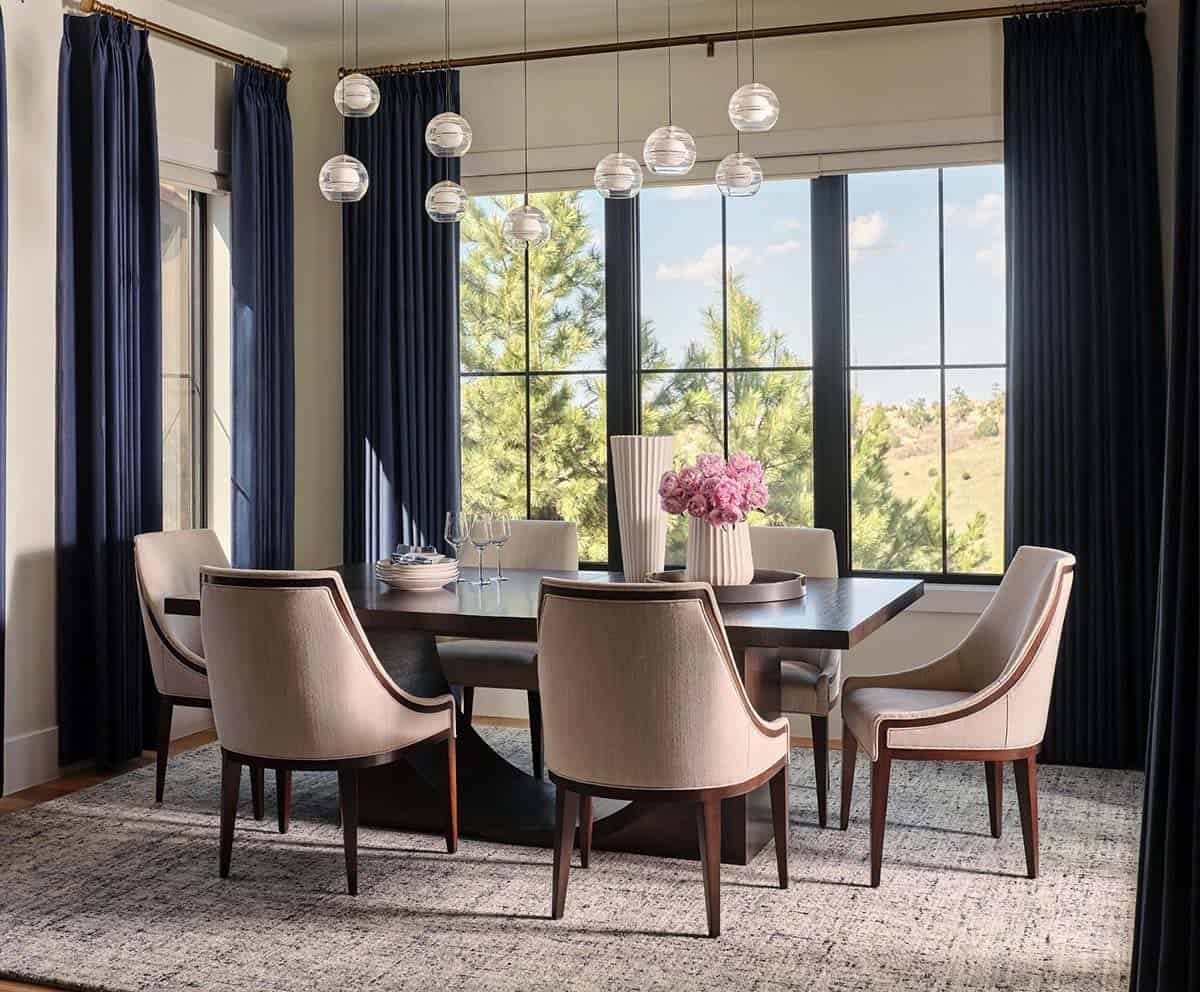 Dining room with dark wood table, cream upholstered chairs, globe pendant lights, and navy floor-to-ceiling curtains