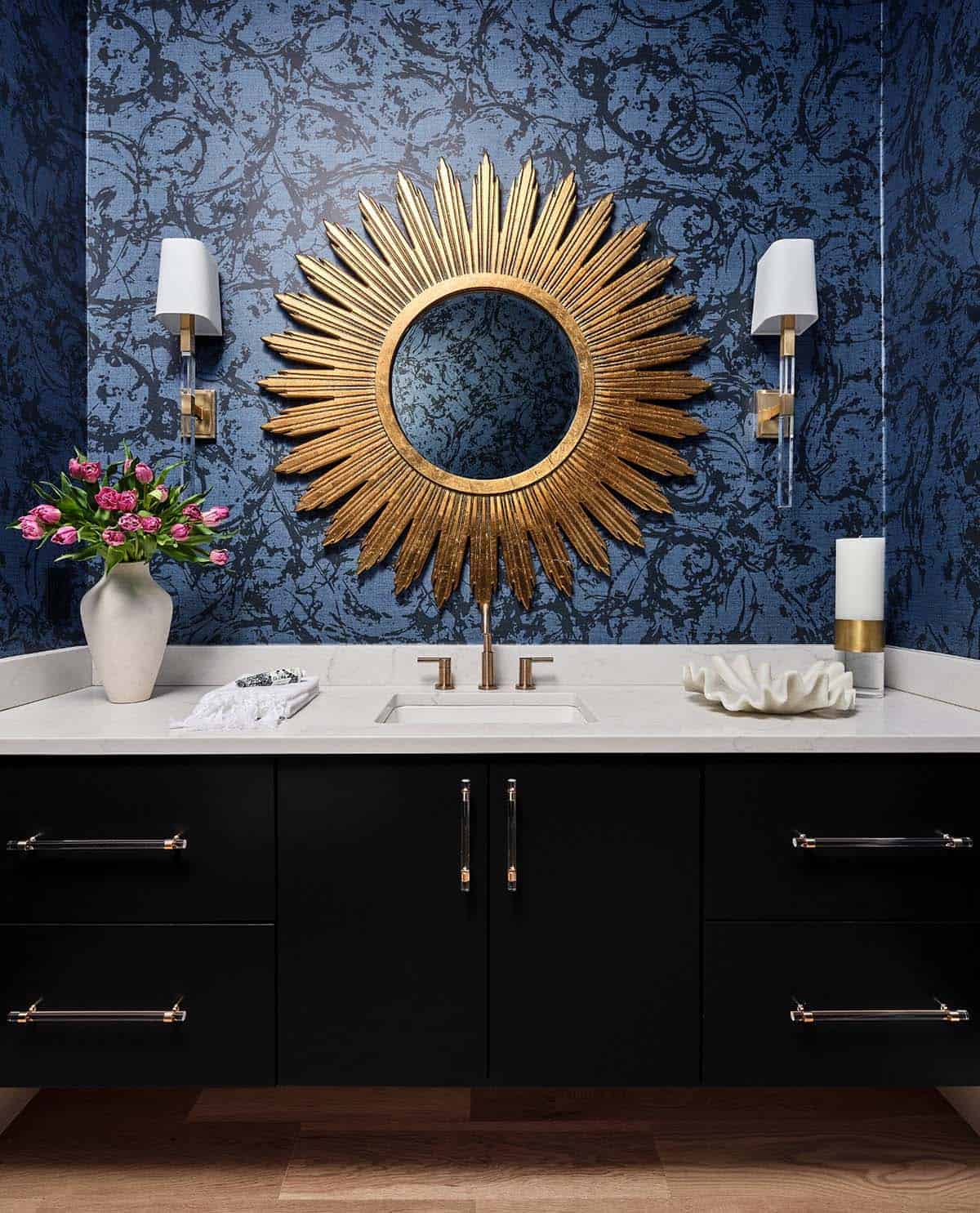 Powder room vanity with sunburst mirror, textured navy wallpaper, black cabinetry, and brass fixtures