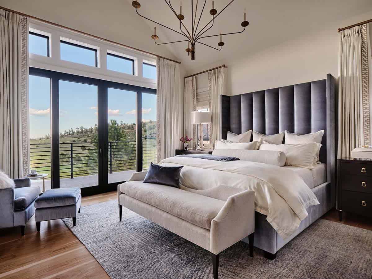 Primary bedroom with tall gray channel-tufted headboard, cream bedding, and French doors to a mountain-view balcony