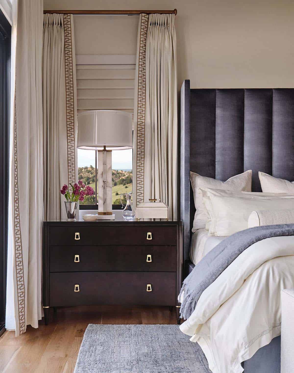 Primary bedroom with tall gray channel-tufted headboard, cream bedding, and French doors to a mountain-view balcony