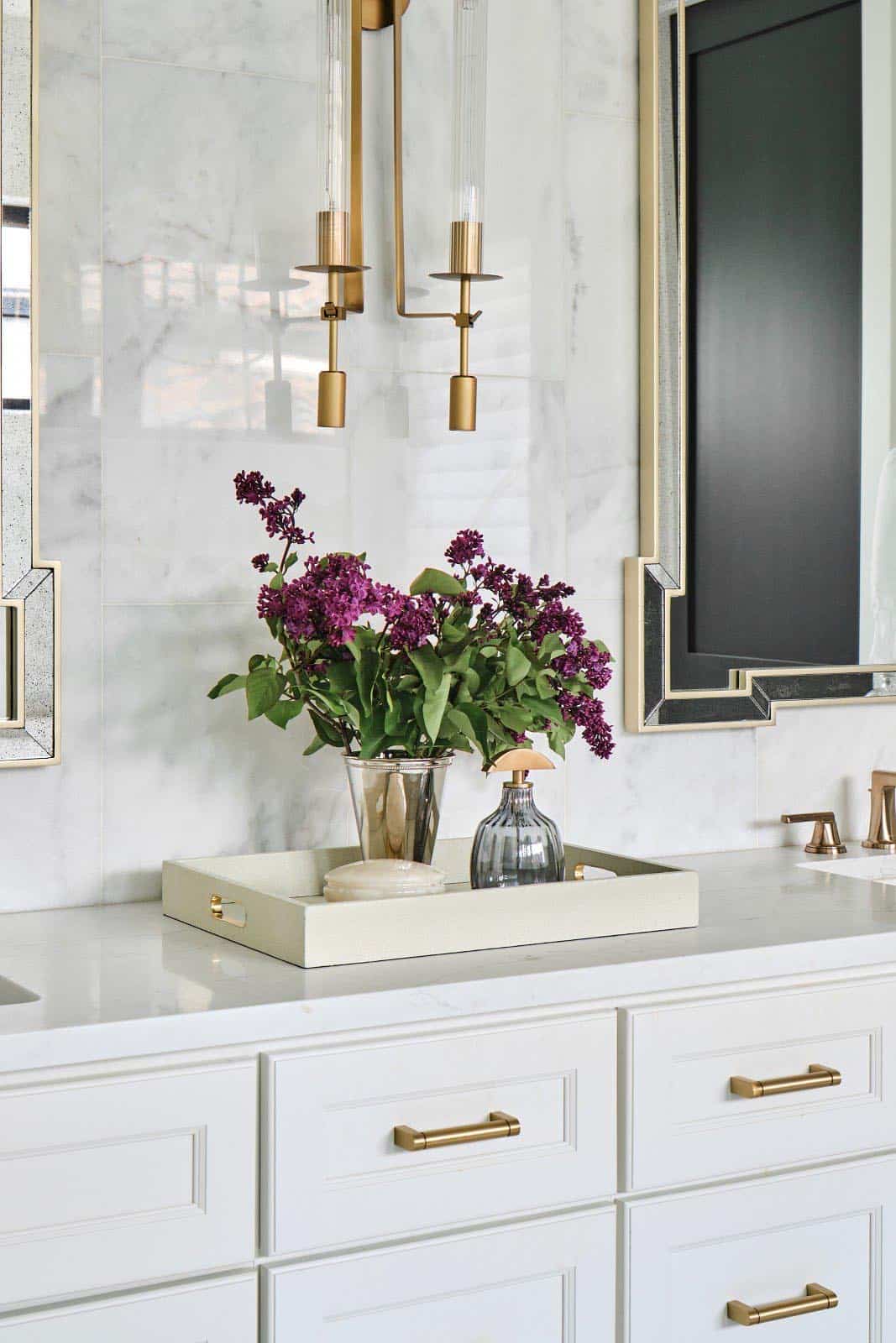 Double vanity bathroom with white cabinetry, marble tile wall, twin brass-framed mirrors, and gold sconces