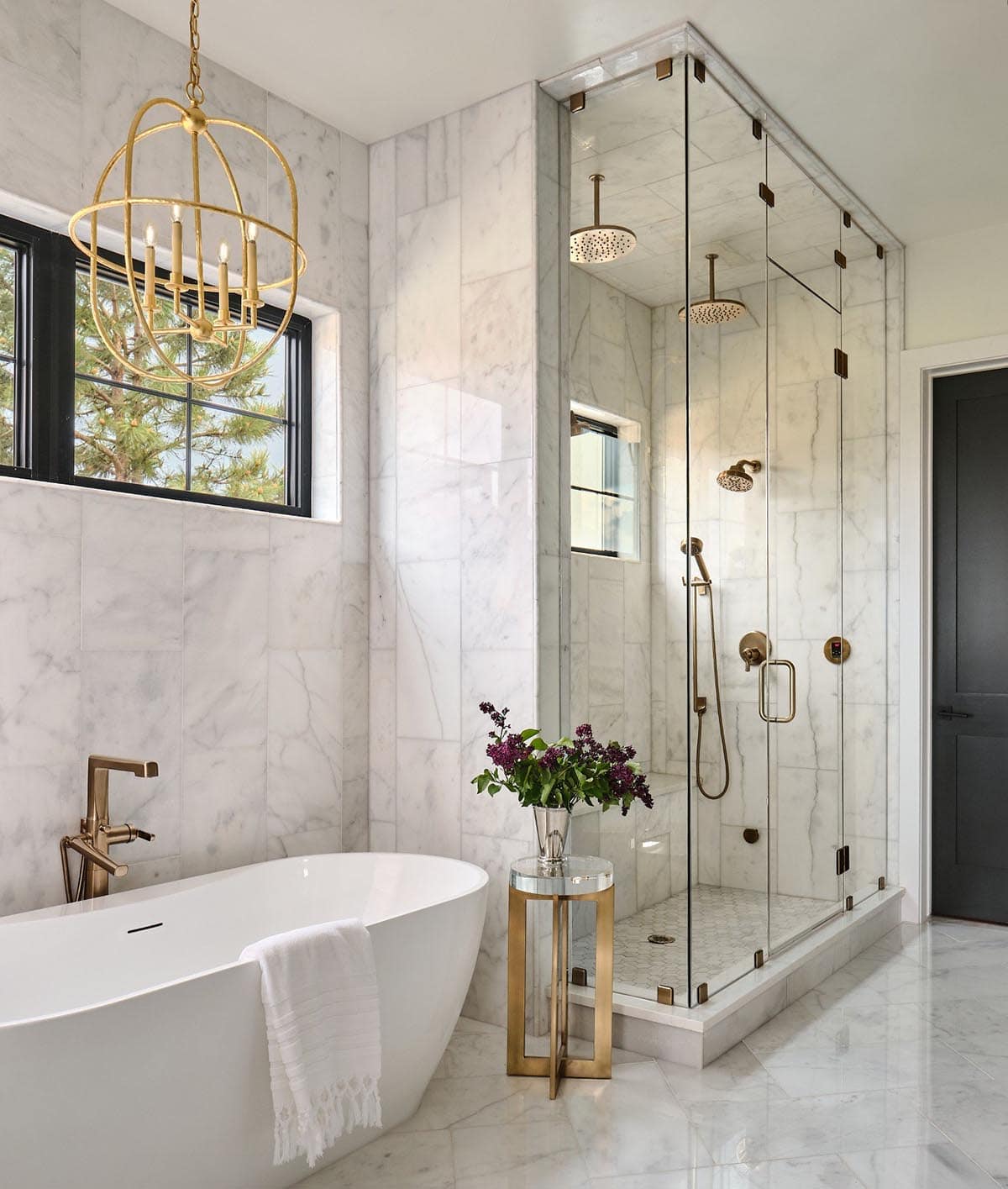 Primary bathroom with freestanding soaking tub, glass-enclosed shower with dual rainheads, and gold globe chandelier