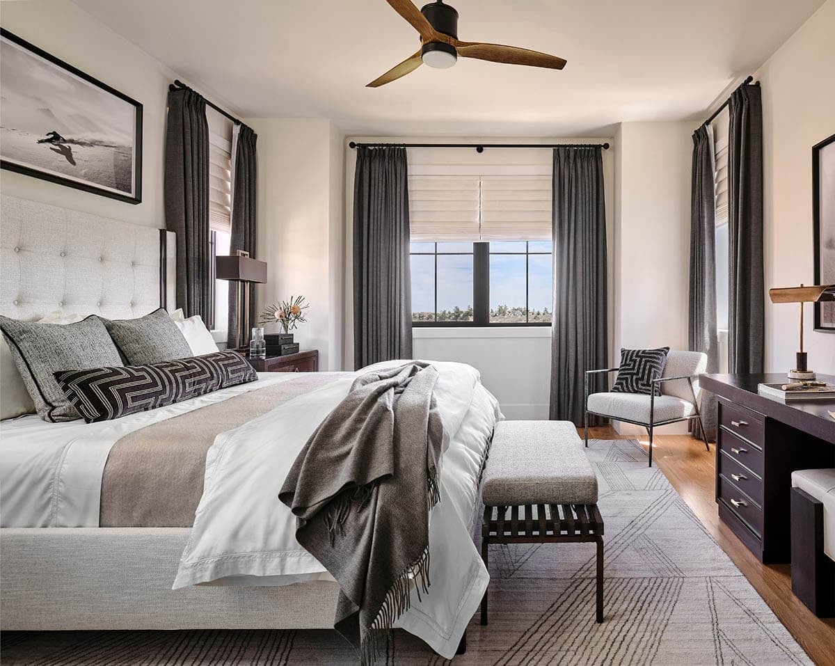 Guest bedroom with tufted cream headboard, wood ceiling fan, dark curtains, and geometric patterned rug