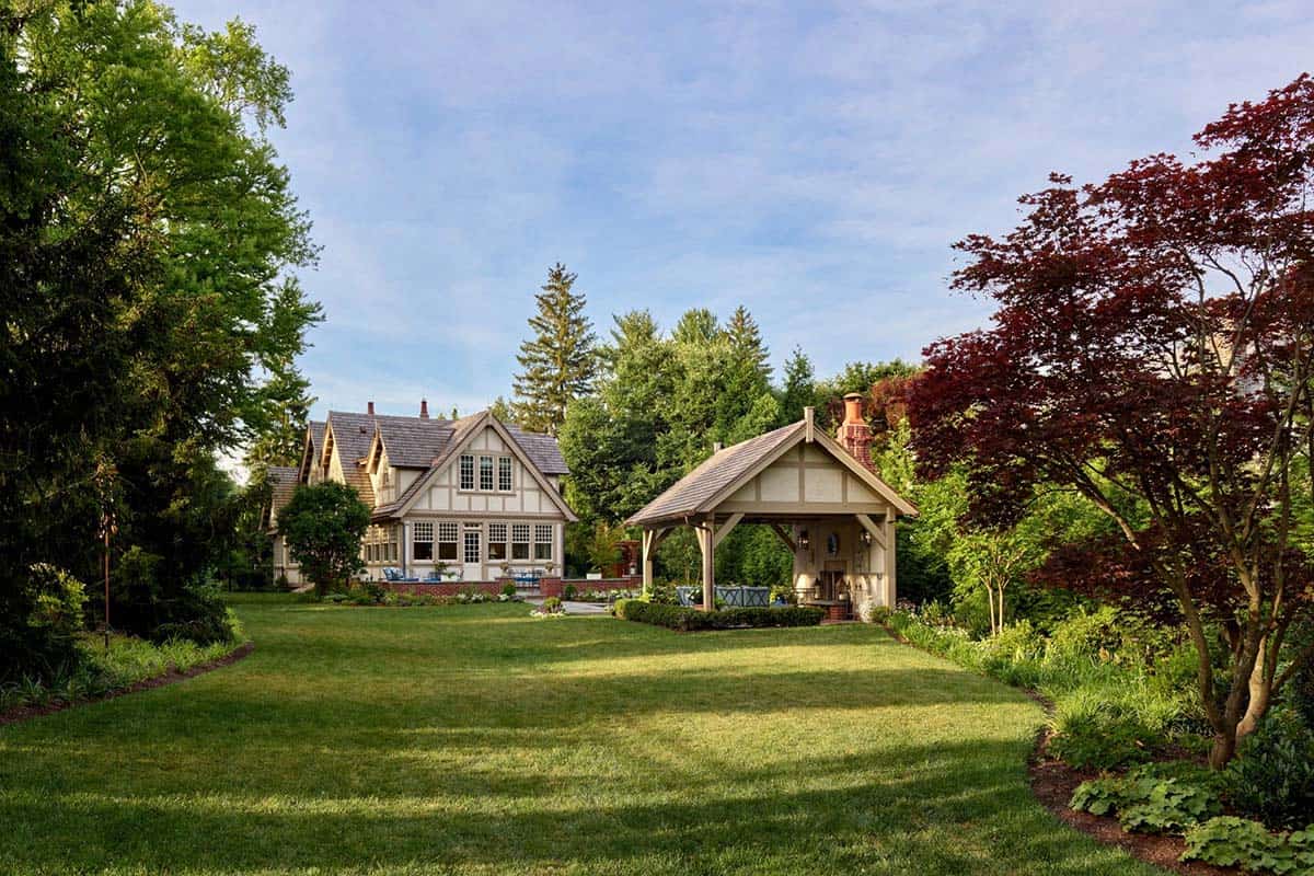 Backyard view of the Tudor home with a timber-framed pavilion beside a green lawn