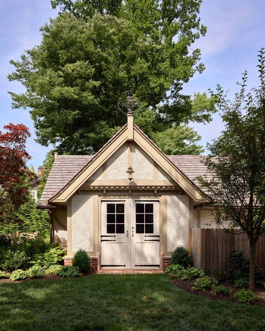 Small stucco outbuilding with a peaked gable roof, weathervane, and double carriage-style doors