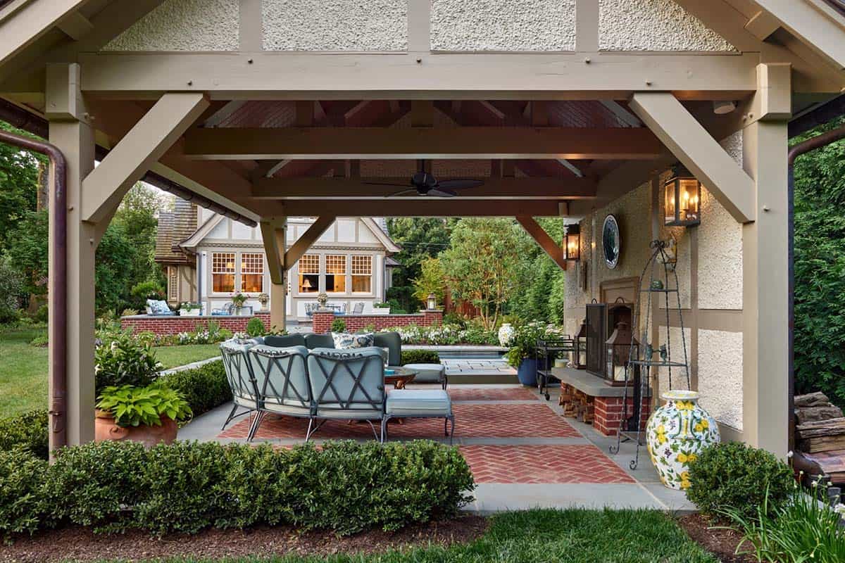 Covered outdoor living area with seating, fireplace, and lantern lighting overlooking the pool