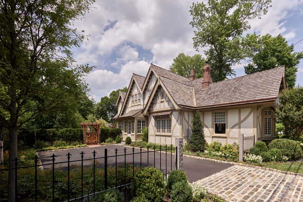 Driveway view of the Tudor house with iron gate, gabled rooflines, and landscaped entrance