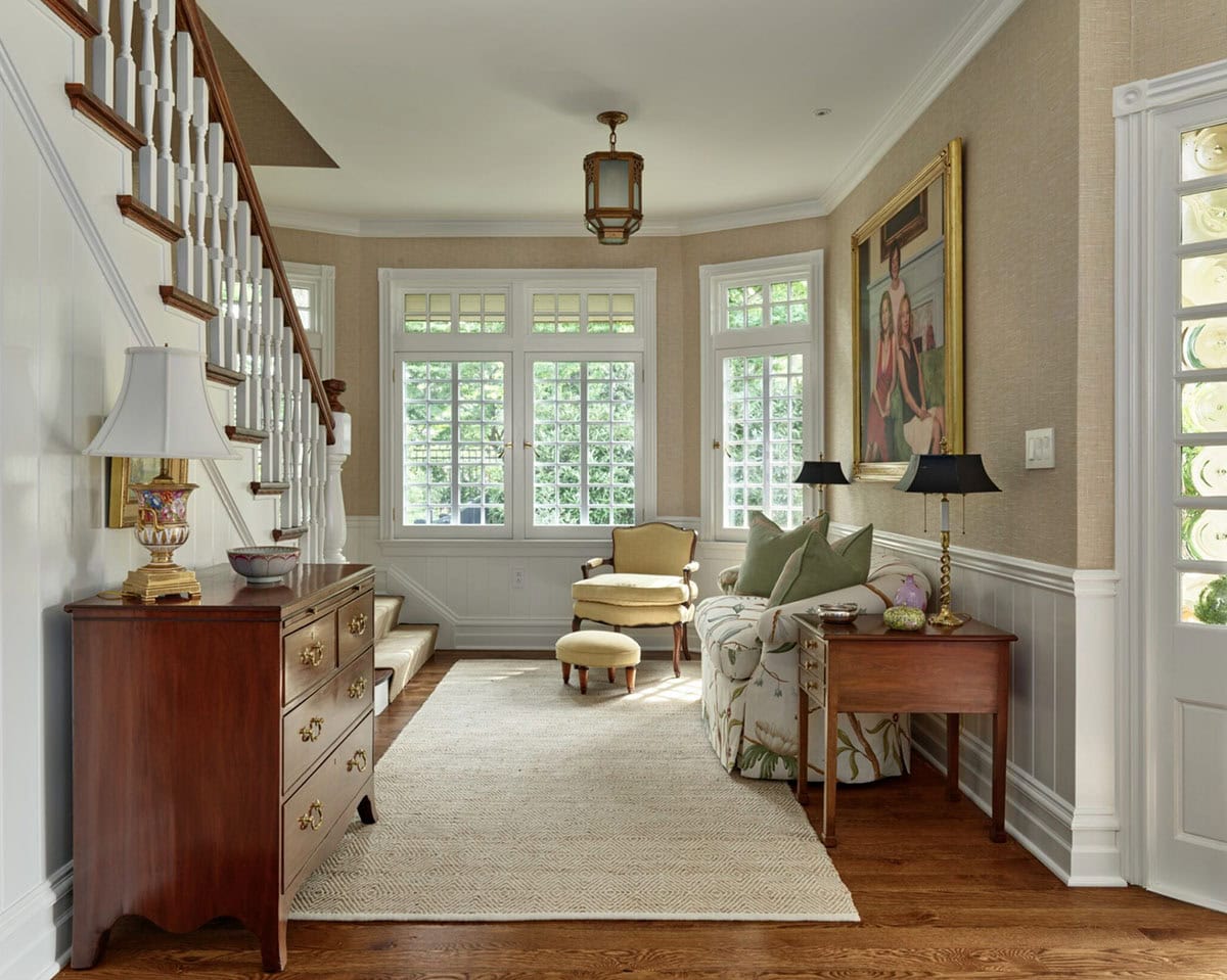 Entryway with staircase, antique wood dresser, upholstered armchair, and multi-pane windows