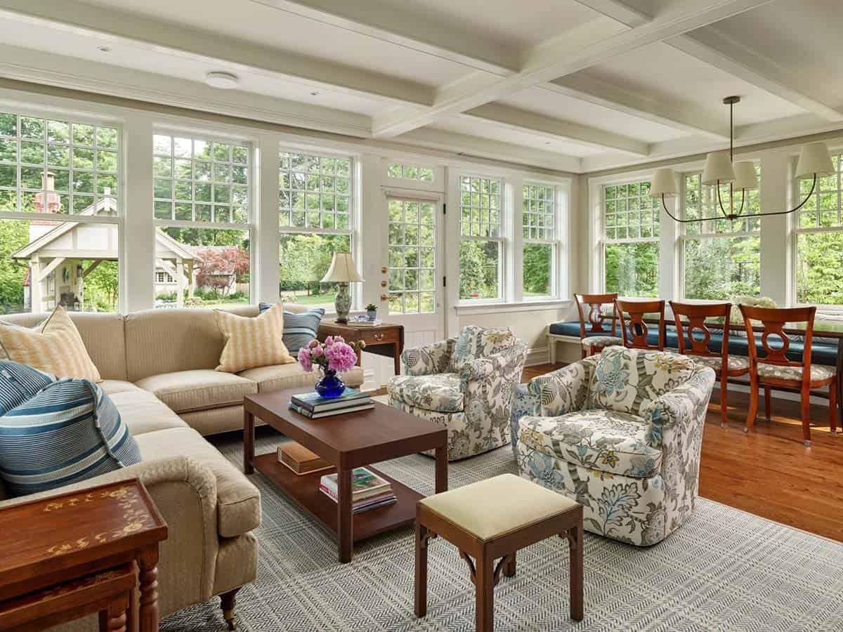 Sunroom with coffered ceiling, floral armchairs, sectional sofa, and wall of windows