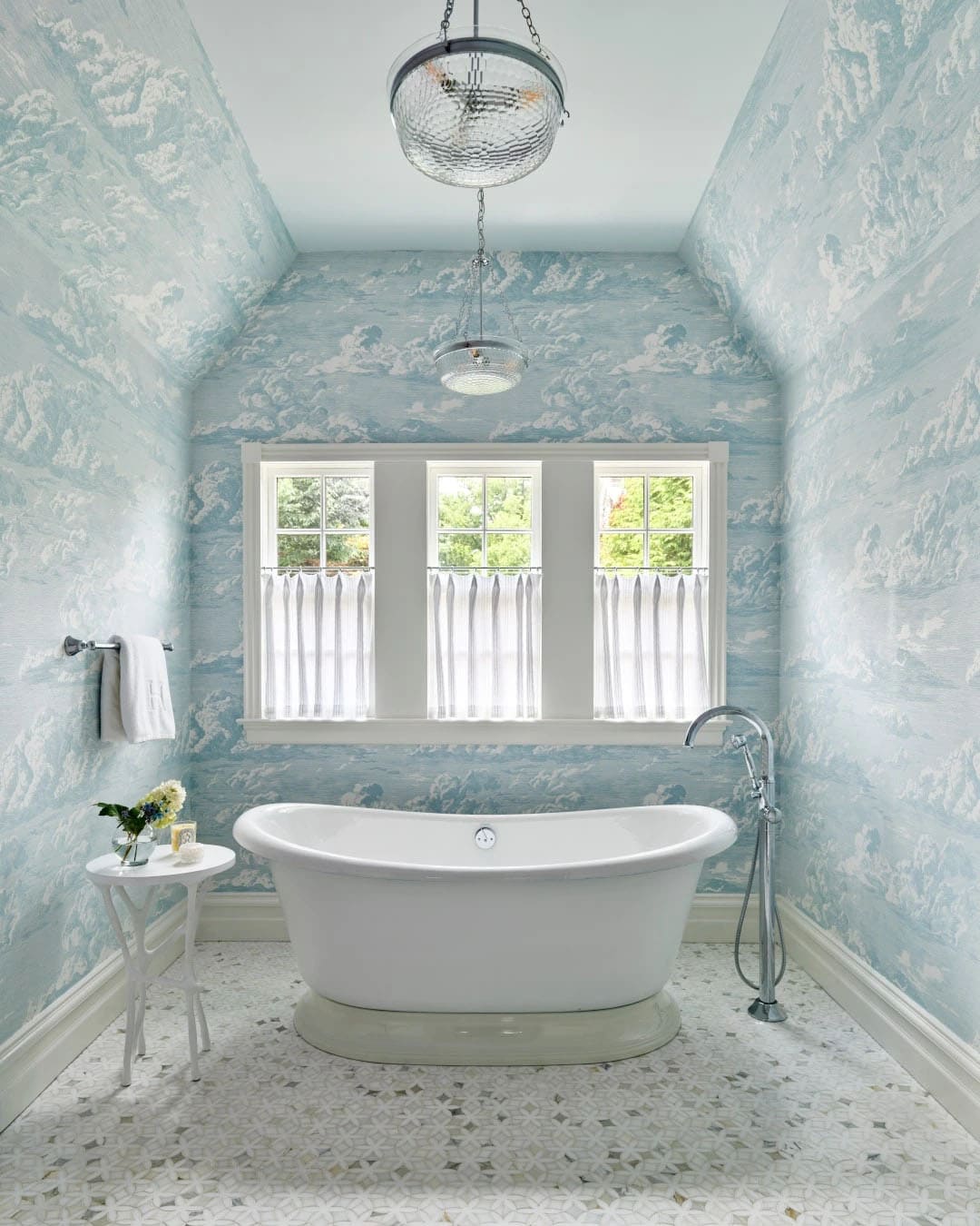 Bathroom with cloud-patterned blue wallpaper, freestanding tub, and mosaic tile floor