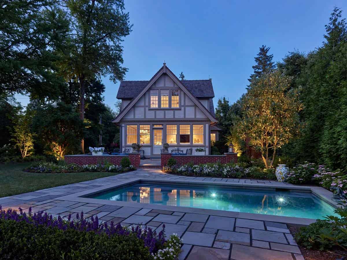 Illuminated Tudor guest cottage at dusk, reflected in the adjacent swimming pool
