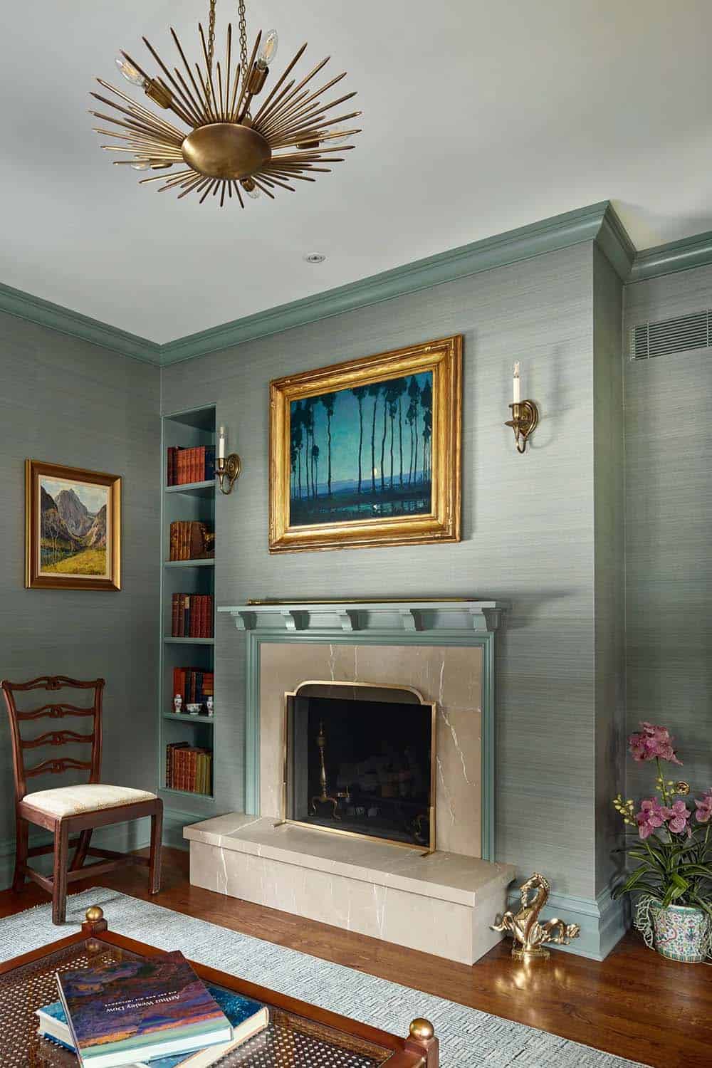 Sitting room with sage-blue walls, marble fireplace, gilt-framed art, and starburst chandelier