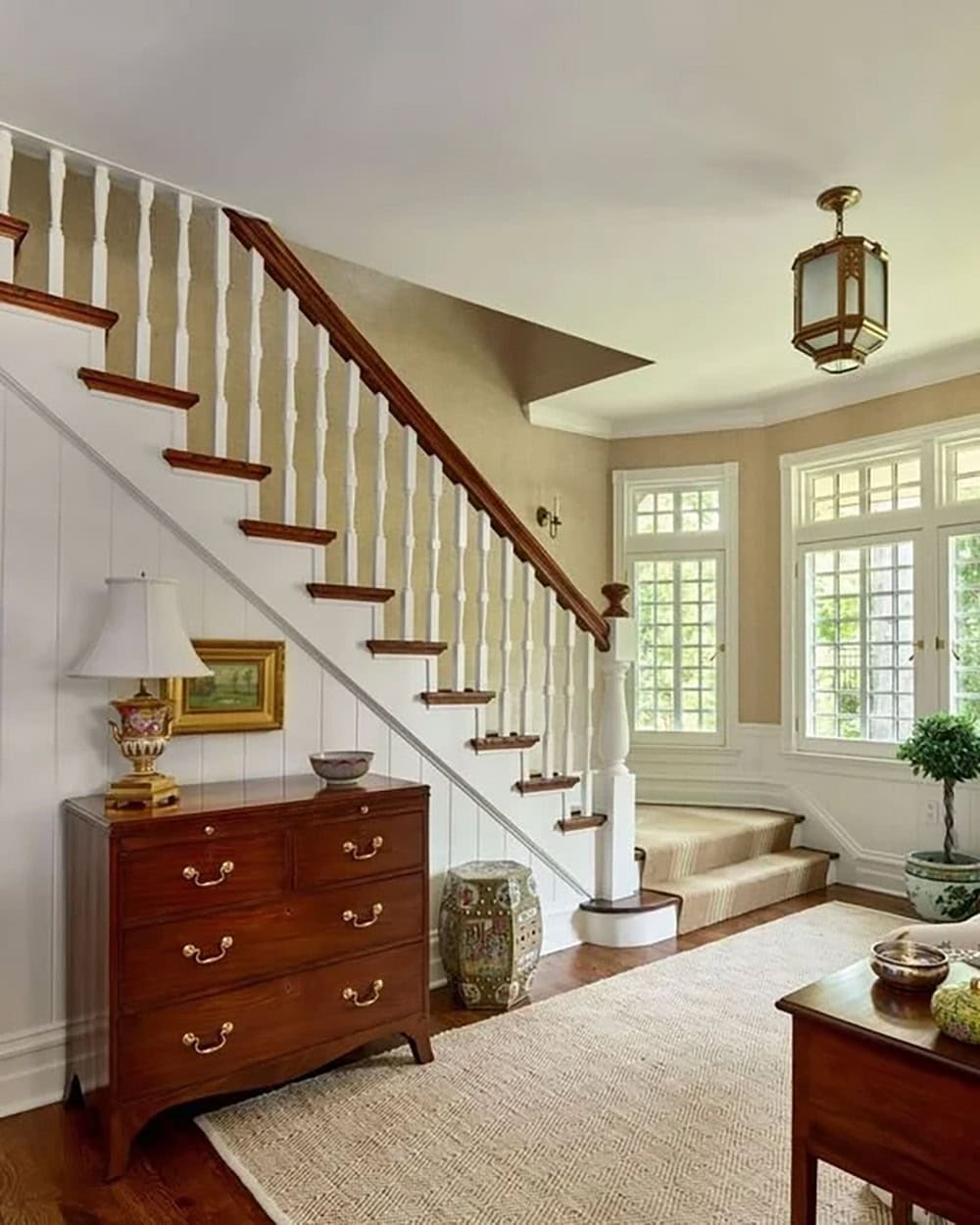 Staircase landing with wood dresser, striped runner, and multi-pane bay windows