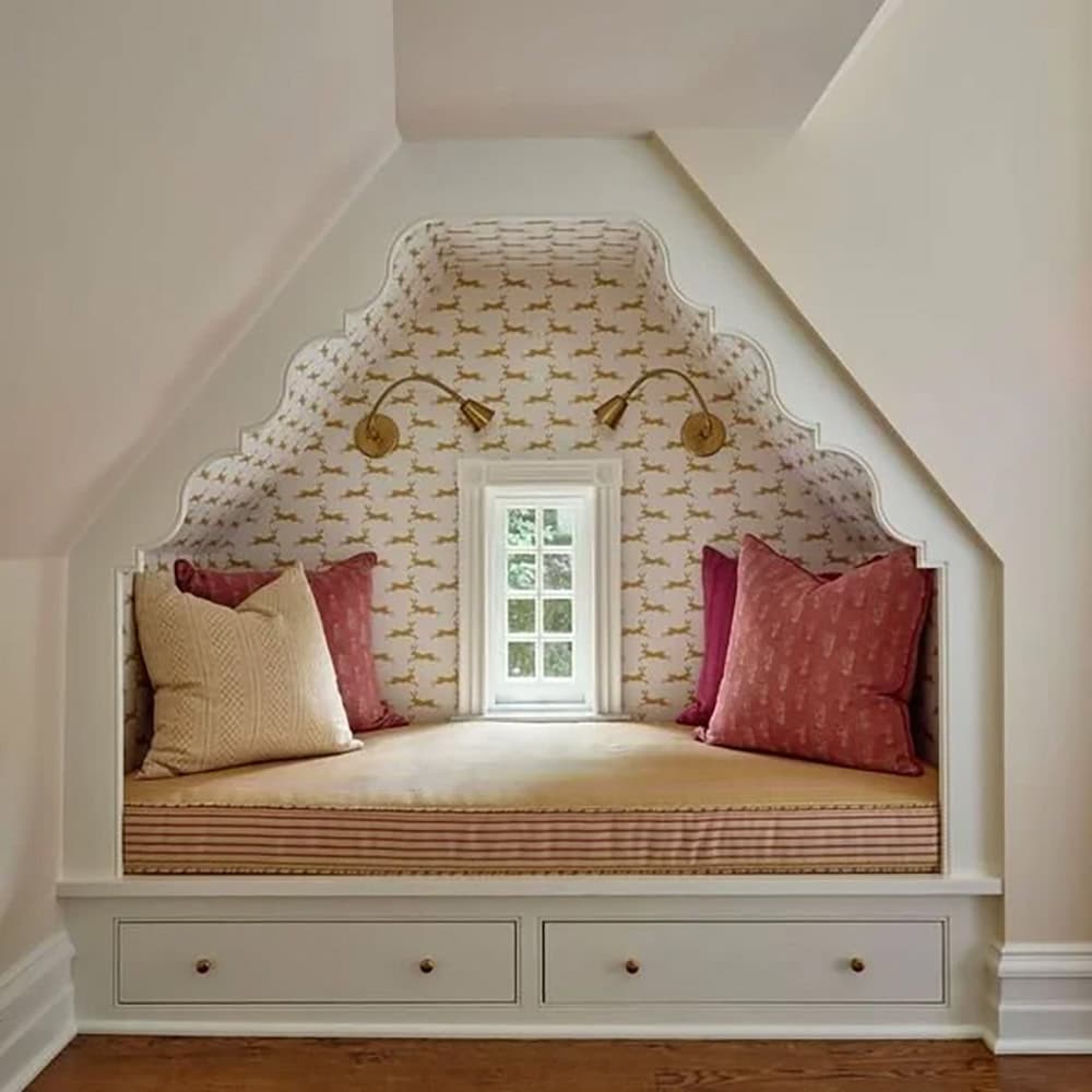 Built-in window seat under the eaves with patterned wallpaper, sconces, and striped cushion