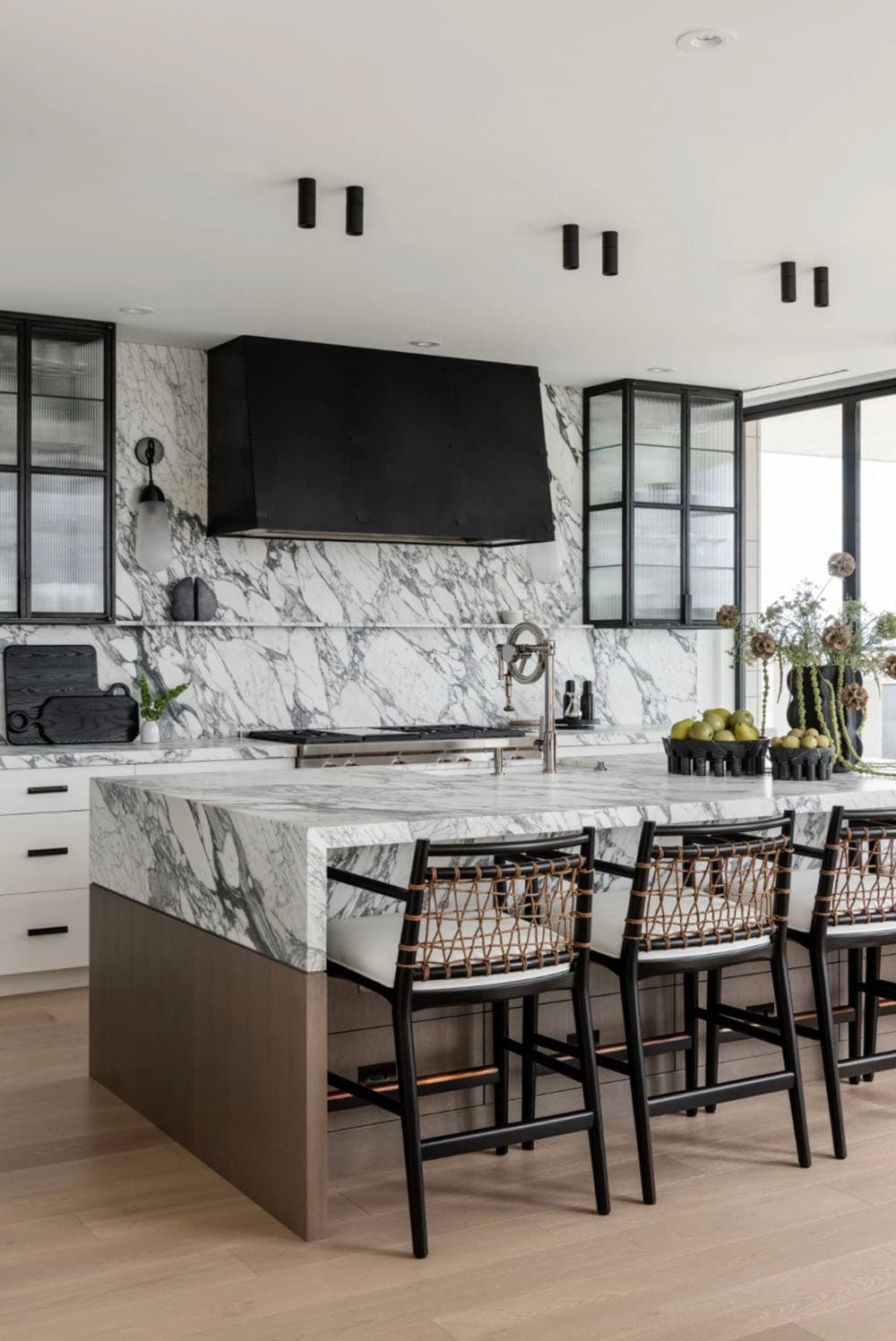 Kitchen island with marble countertop, black bar stools, and reeded glass cabinets