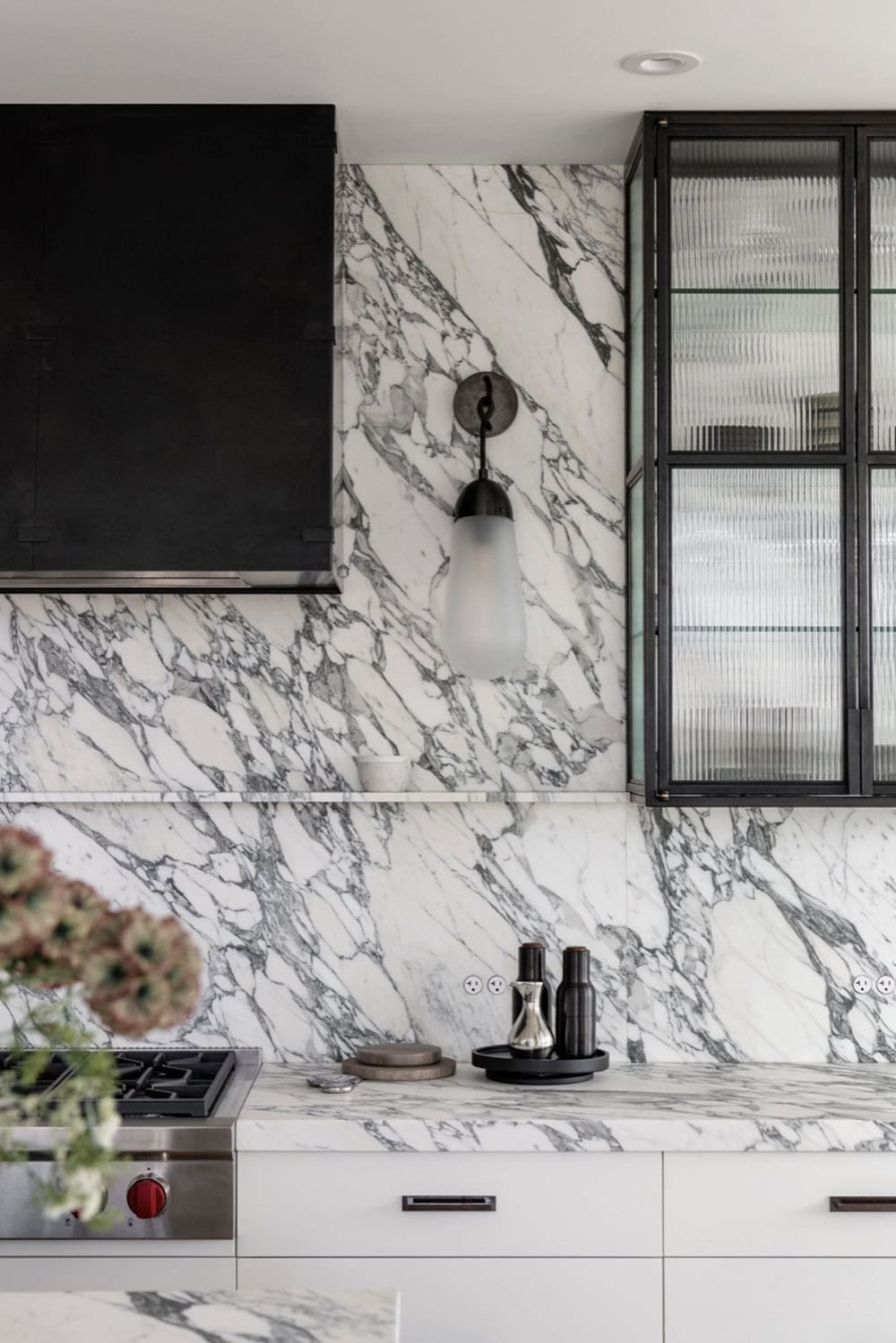 Marble backsplash detail with sconce lighting and reeded glass cabinet