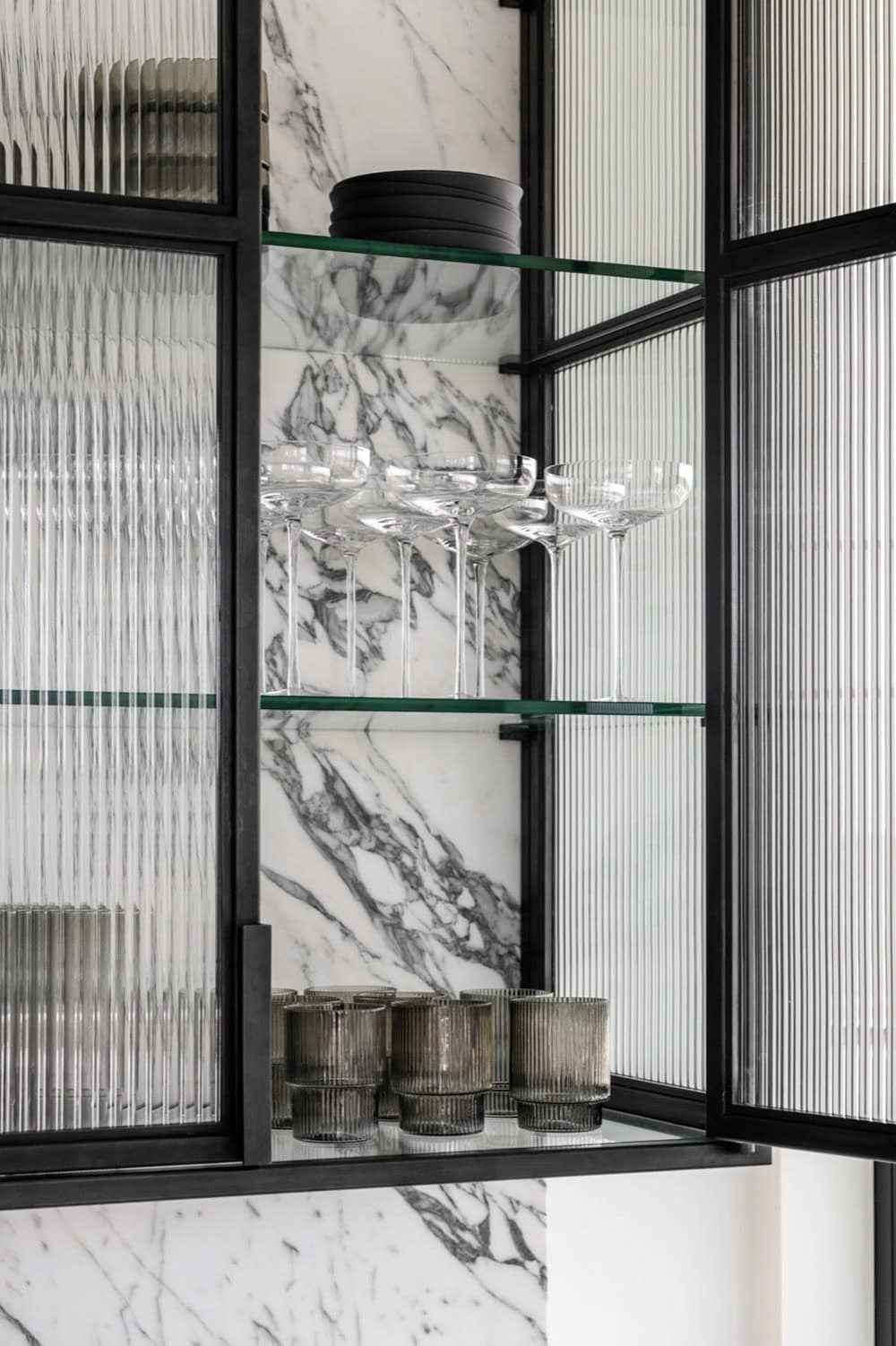 Reeded glass cabinet with glassware and marble backsplash detail