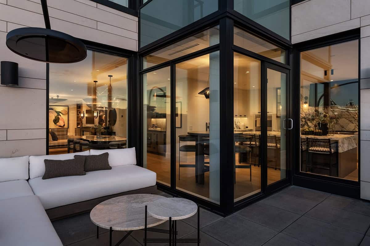 Terrace lounge with glass-walled kitchen and dining views at dusk