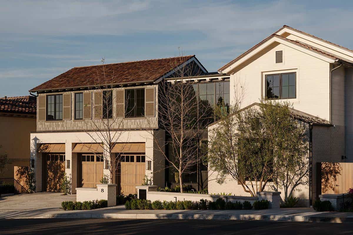 Exterior view of white brick contemporary home with wood garage doors and cedar shingle roof