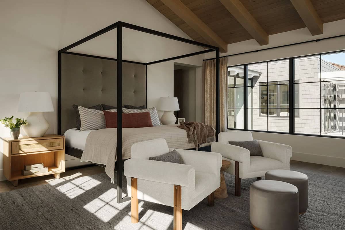 Primary bedroom with a canopy bed, chairs and large windows