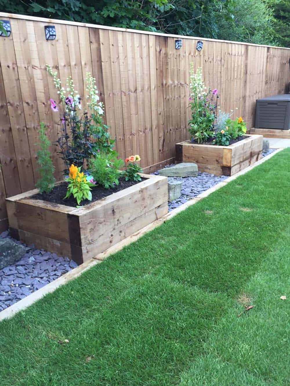 Wood planter boxes filled with cottage flowers along a fence with slate gravel border