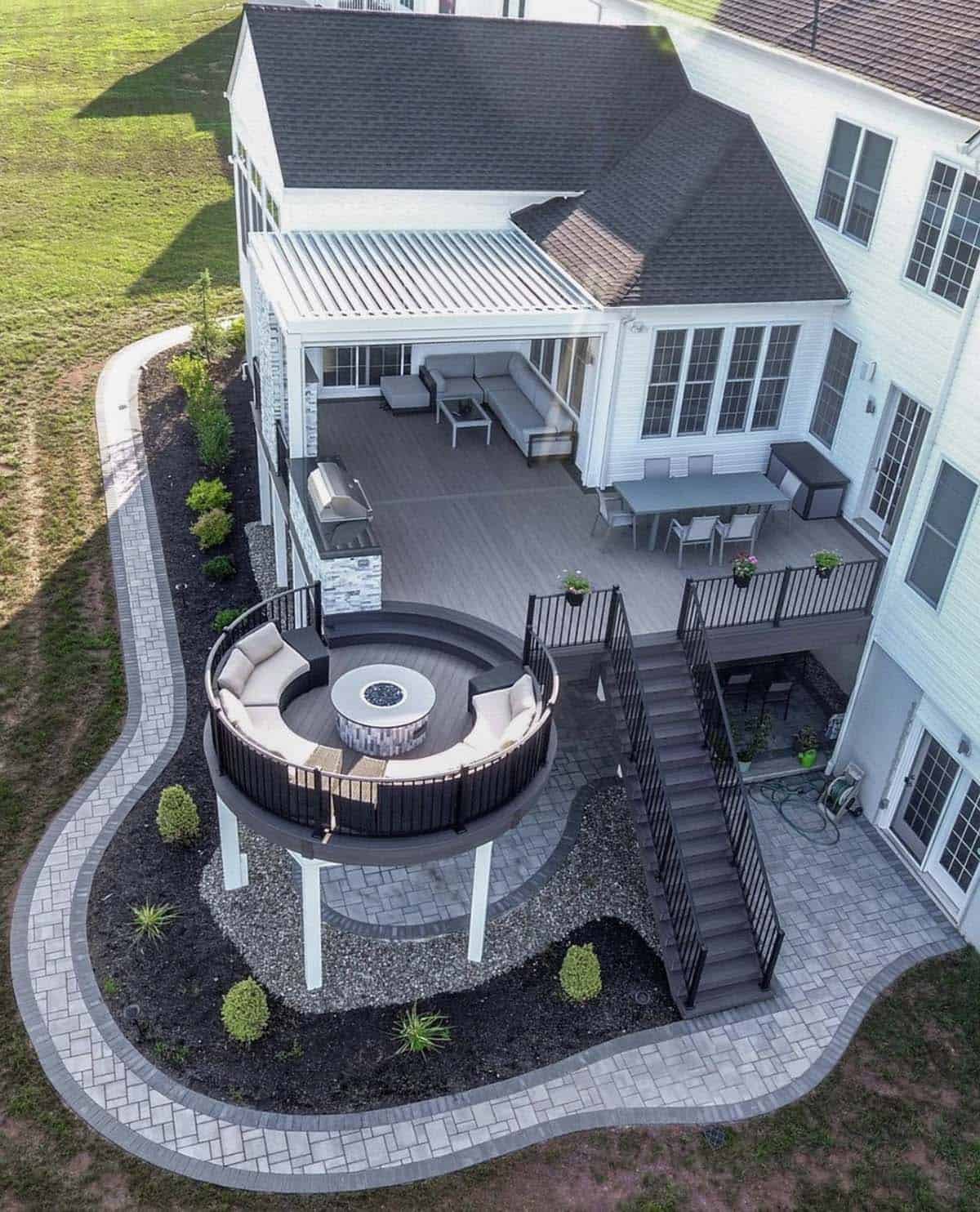 Aerial view of multi-level deck with round cantilevered fire pit lounge, pergola, and outdoor kitchen