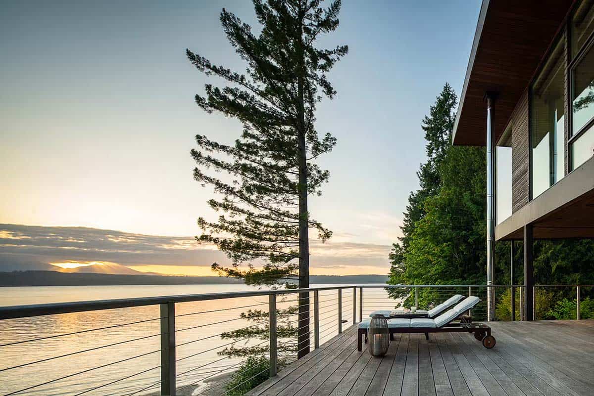 Sunset over water from house deck with lounge chairs, tall pine tree silhouette in foreground