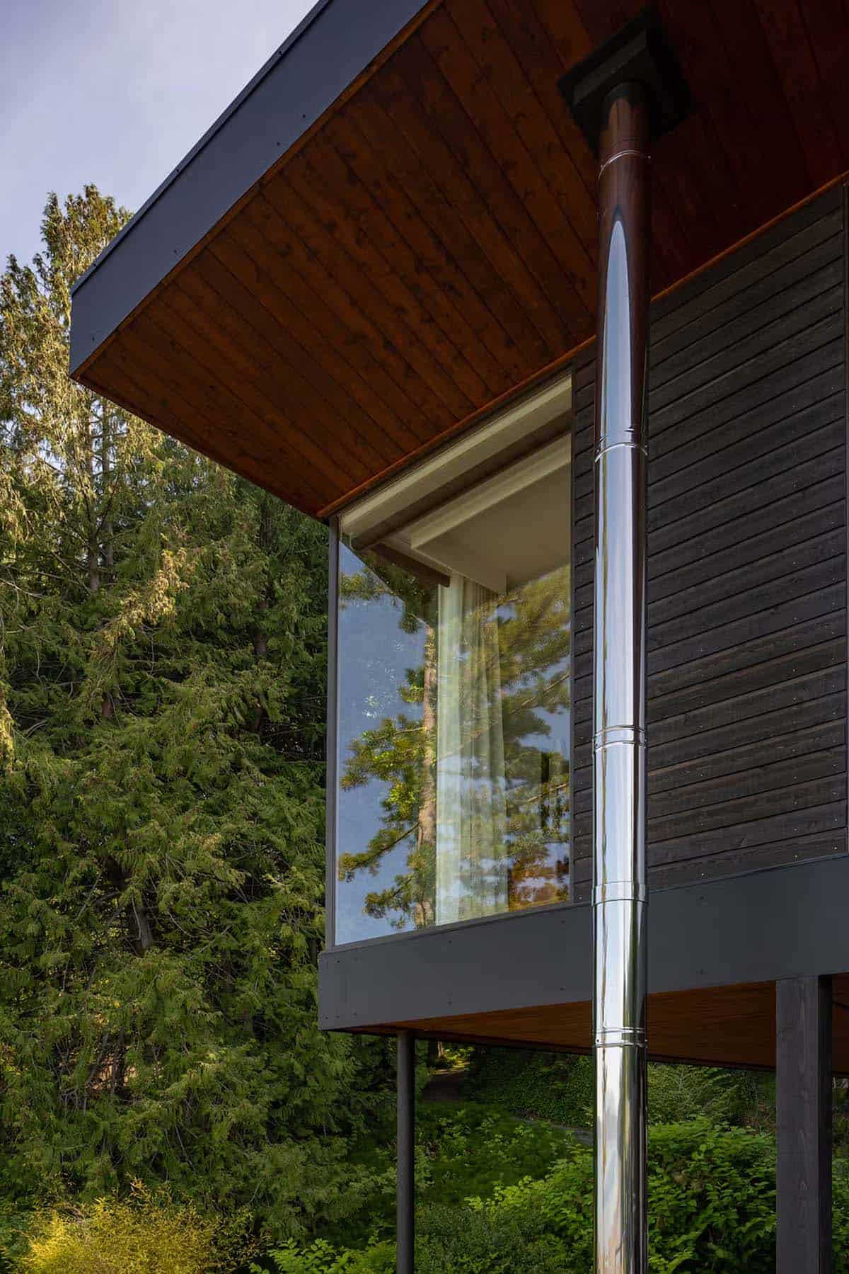 Close-up of cantilevered roof corner with polished metal chimney pipe against dark wood siding