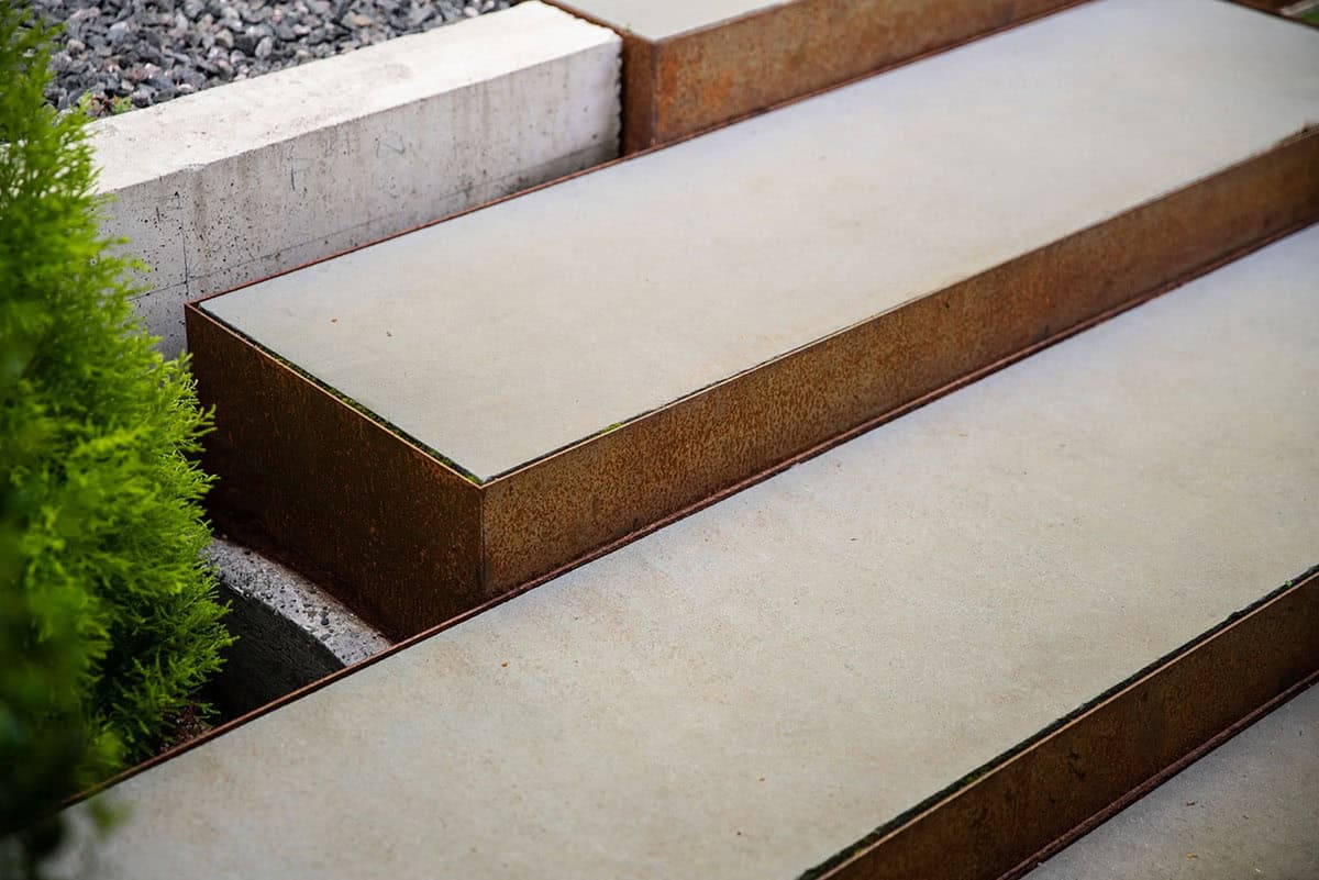 Close-up of Corten steel-edged concrete steps bordered by trimmed greenery