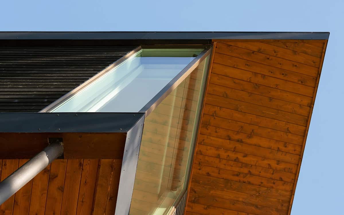 Detail of angled skylight and wood roof eave meeting dark siding against blue sky