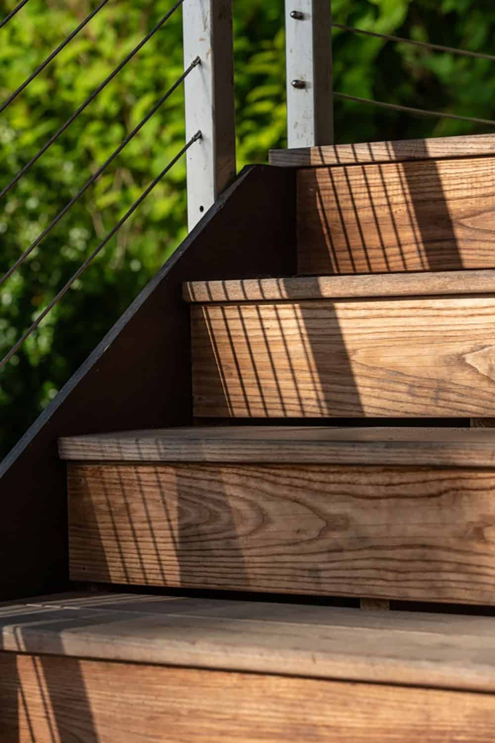Close-up of wooden deck stairs with dappled cable-railing shadows across the treads