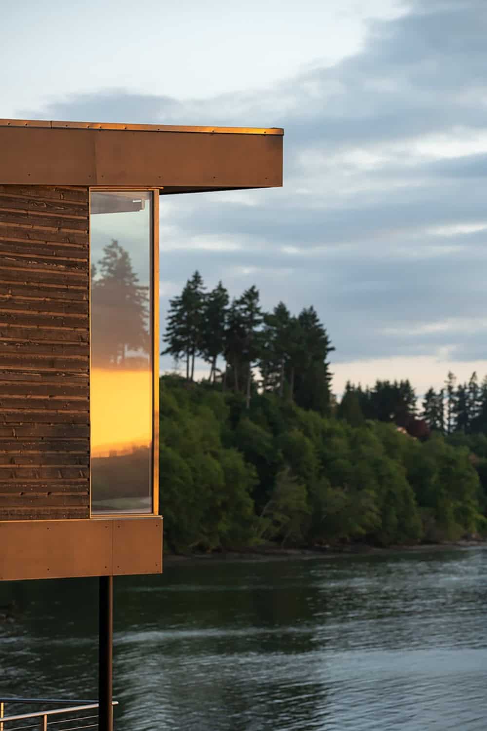 Close-up of wood siding and glass corner window reflecting golden sunset light over the water