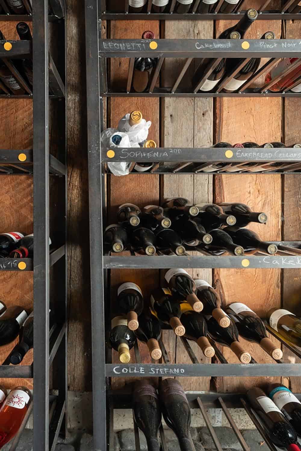 Wine cellar shelving with labeled bottles stored against a rustic wood-plank wall