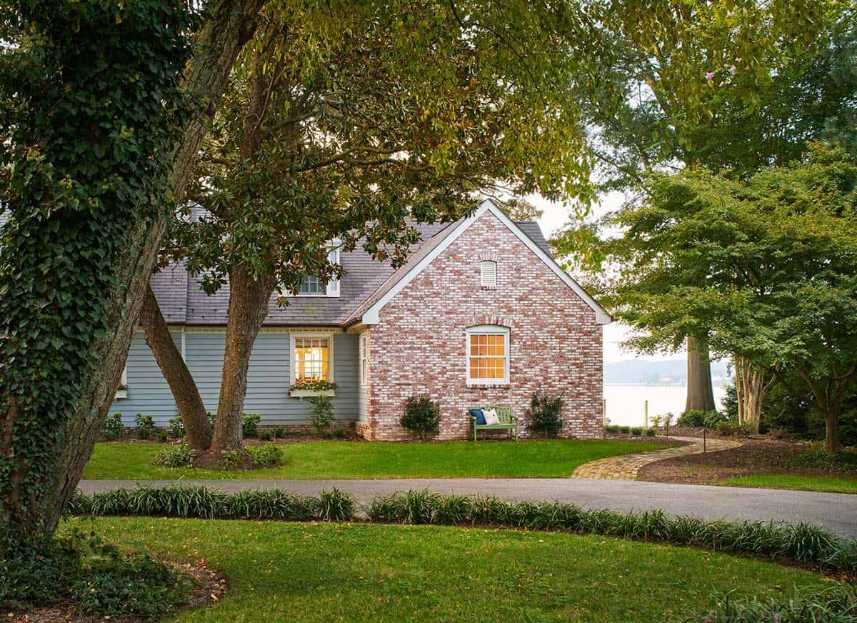 Blue and brick guest cottage exterior with water view through trees