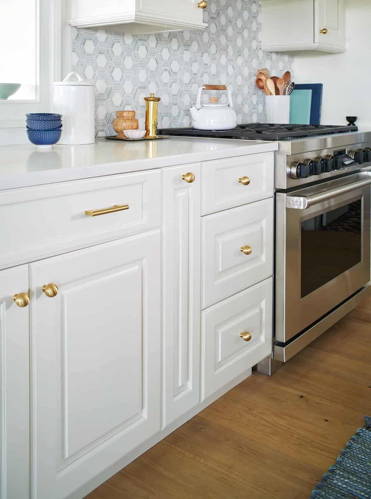 Close-up of white kitchen cabinetry with brass hardware and range