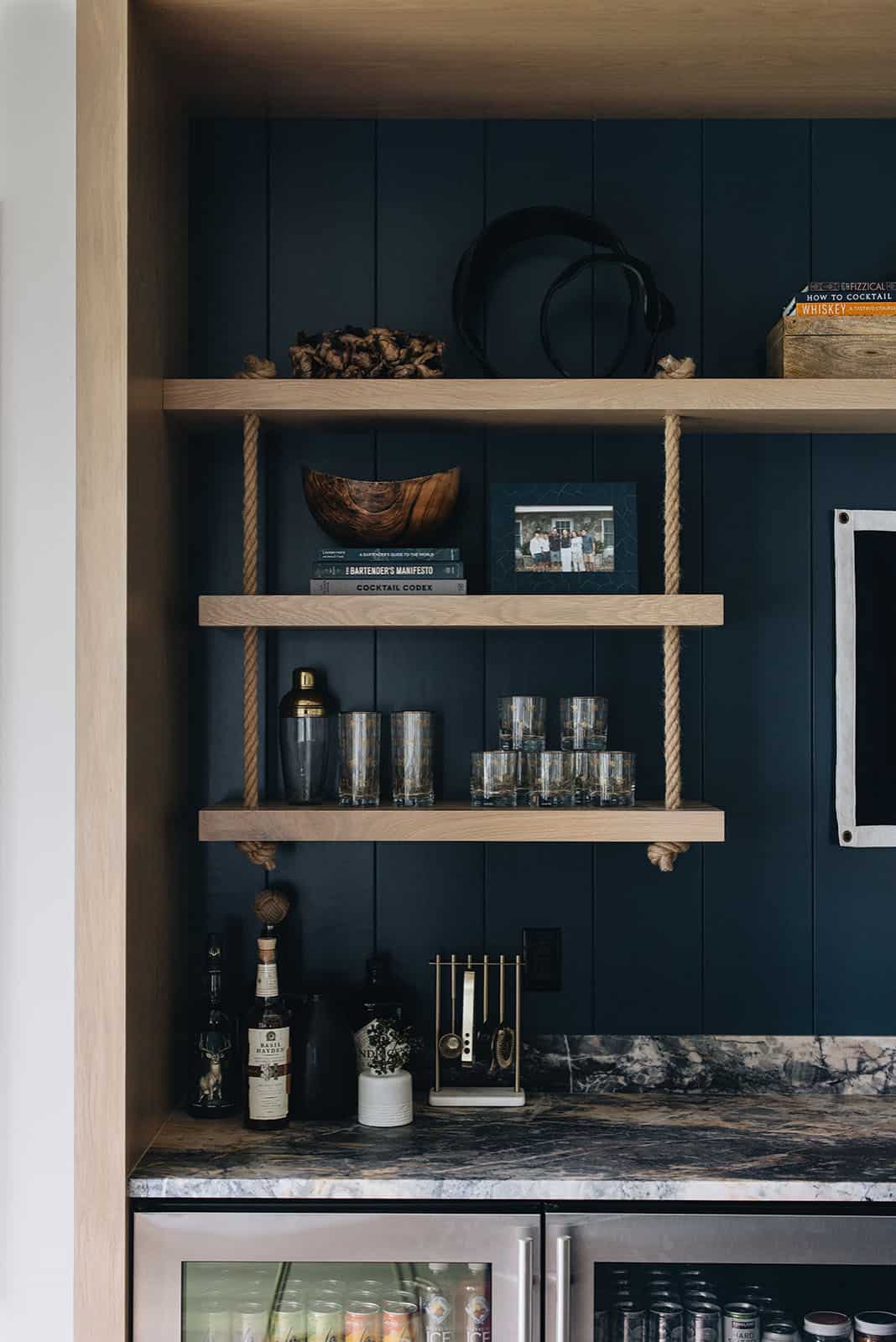 Built-in bar shelving with rope supports, cocktail books, and glassware