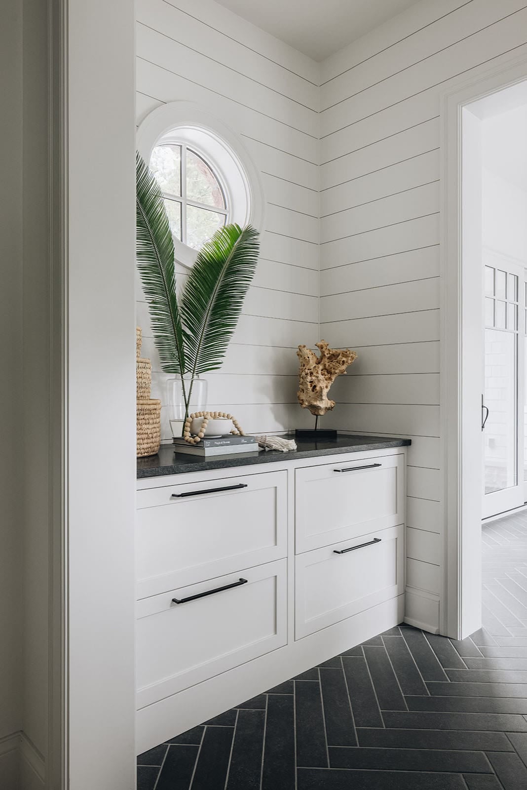 White shiplap mudroom nook with round window and black hardware cabinetry