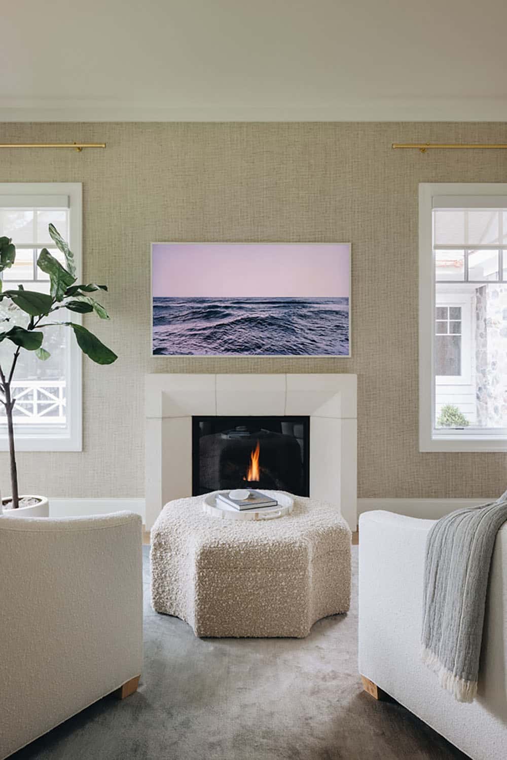Living room seating around fireplace with ocean-view art and boucle ottoman