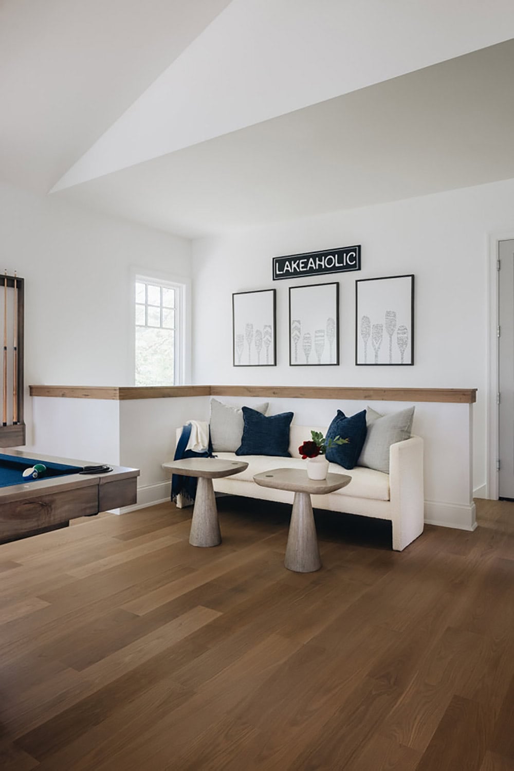 Window seat with "Lakeaholic" sign and framed oar art above pool table railing