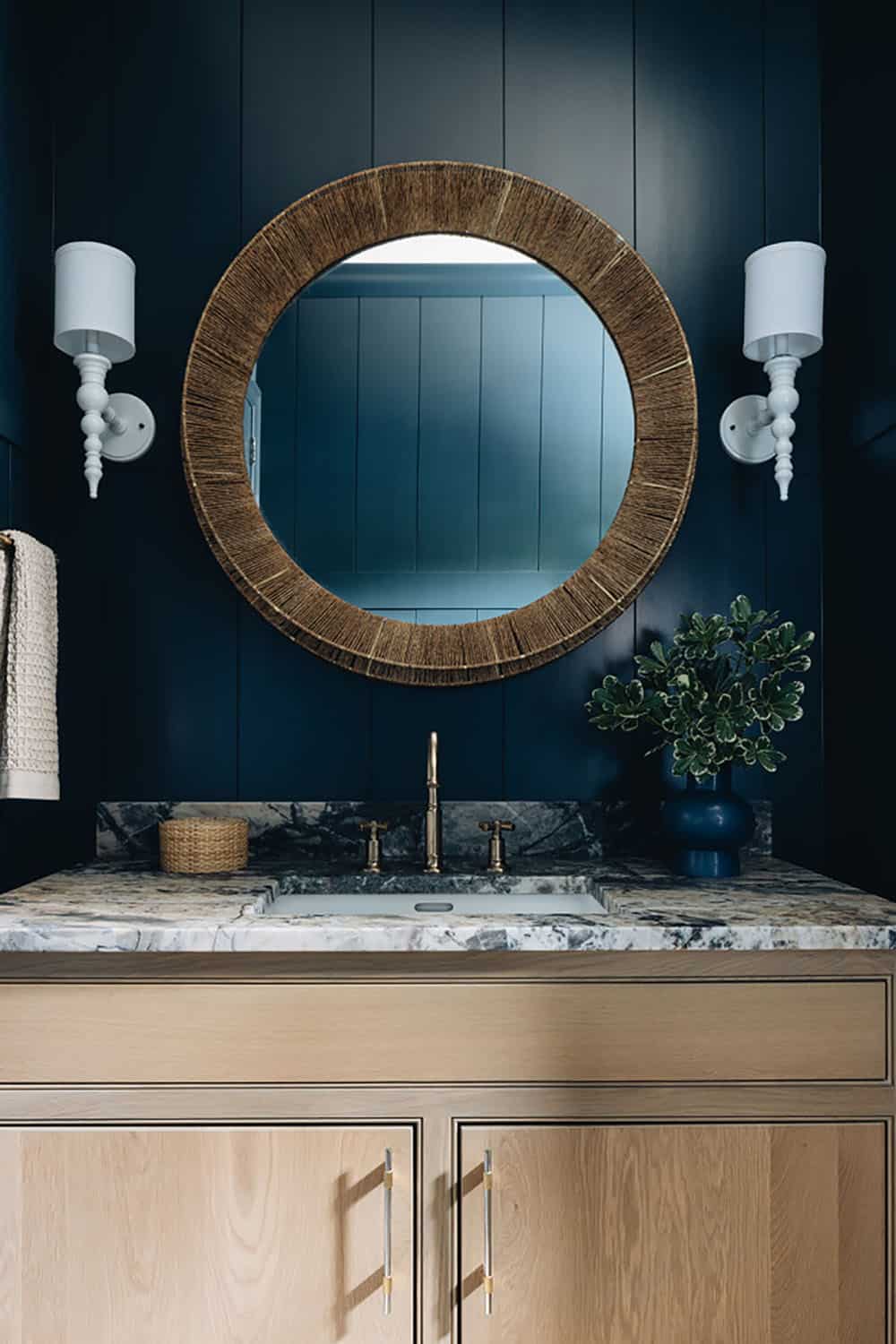 Powder room vanity with round woven mirror against navy shiplap wall