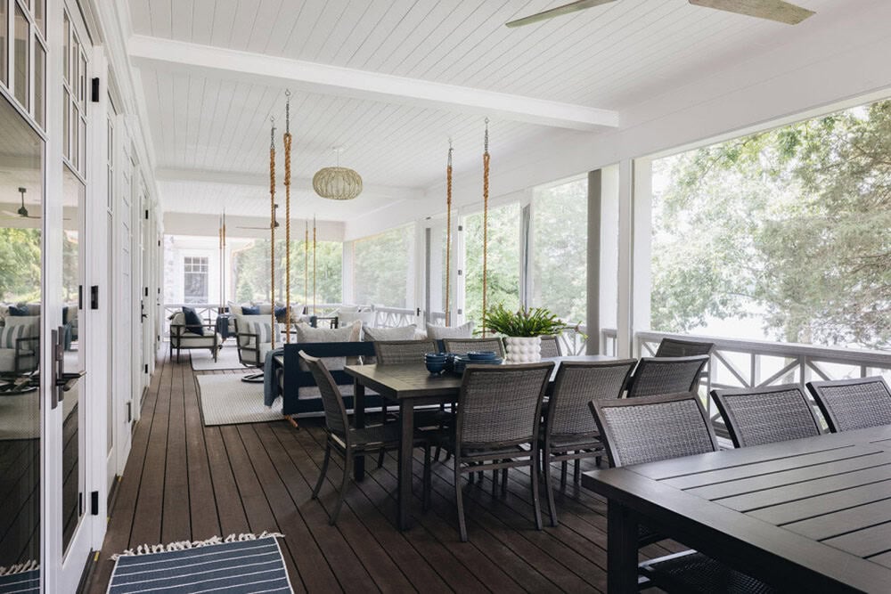 Screened porch with hanging swing, dining table, and lake view