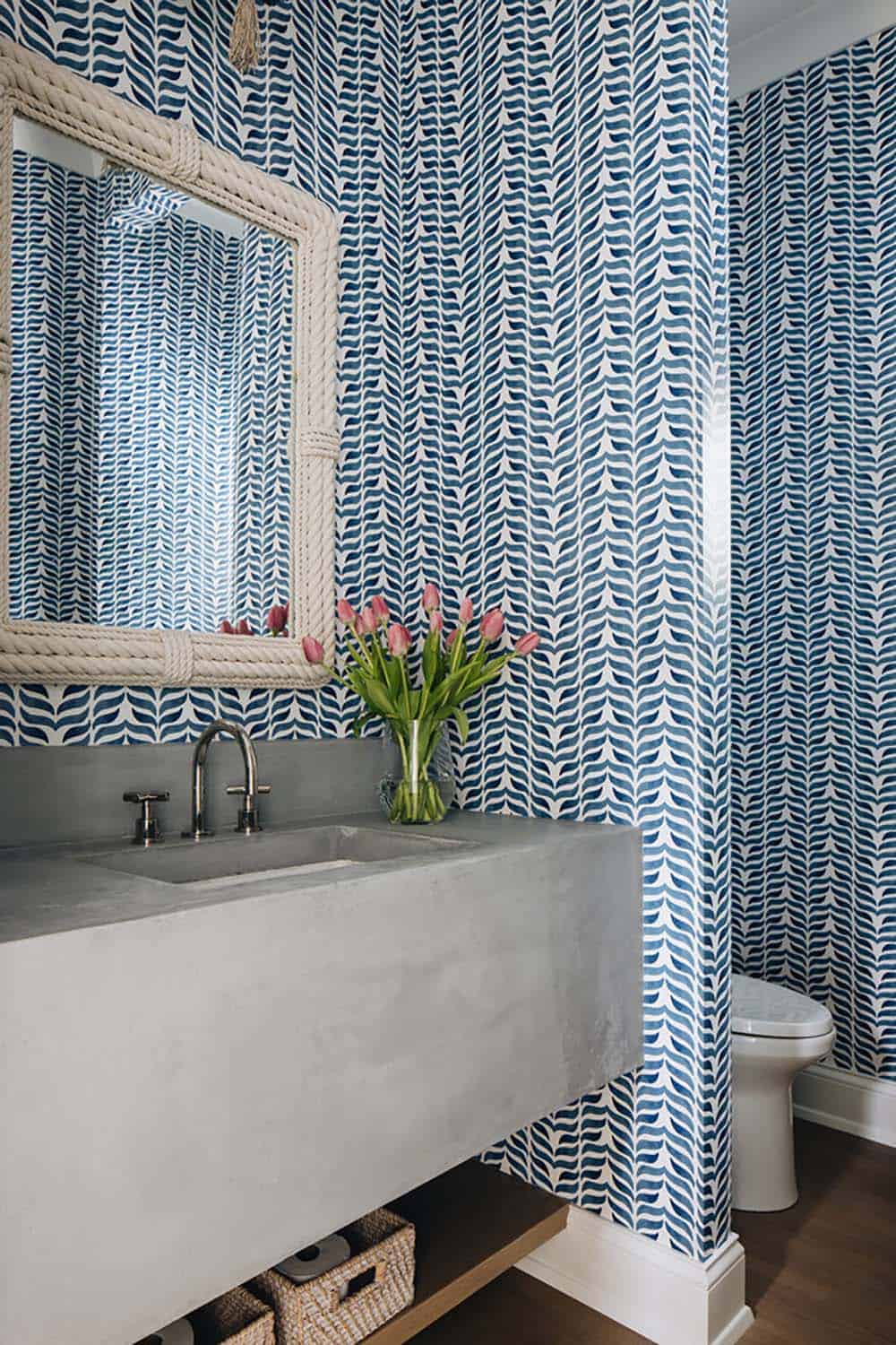 Close-up of blue wallpaper, concrete sink, and rope-framed mirror in powder room