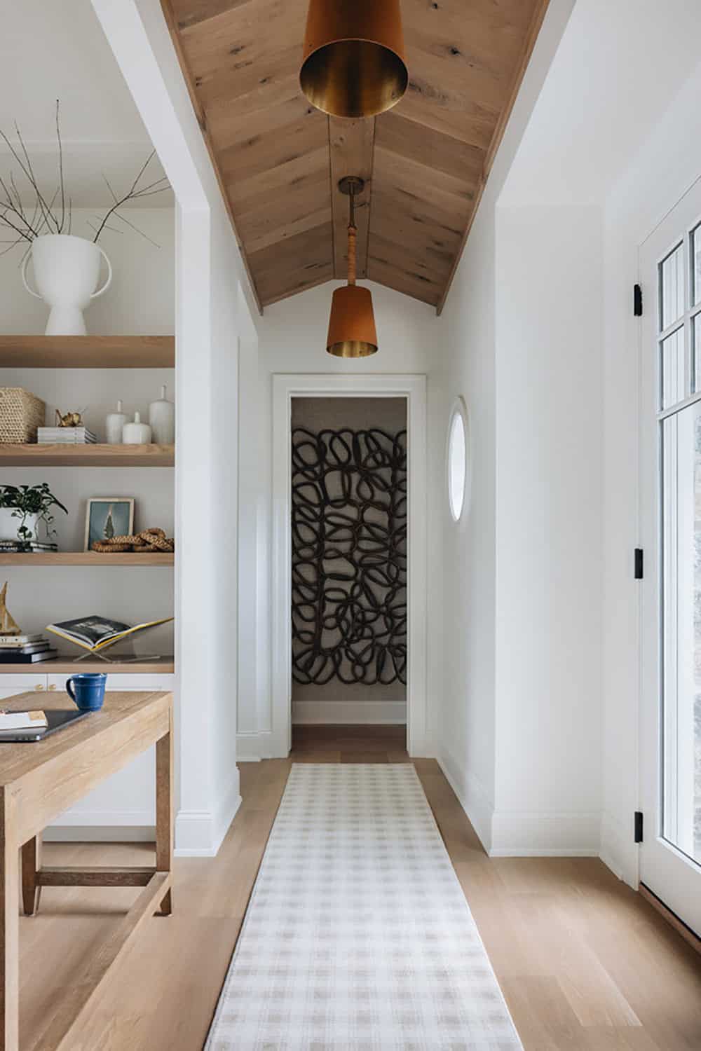 Wood-paneled hallway with brass pendant lights leading to woven wall art