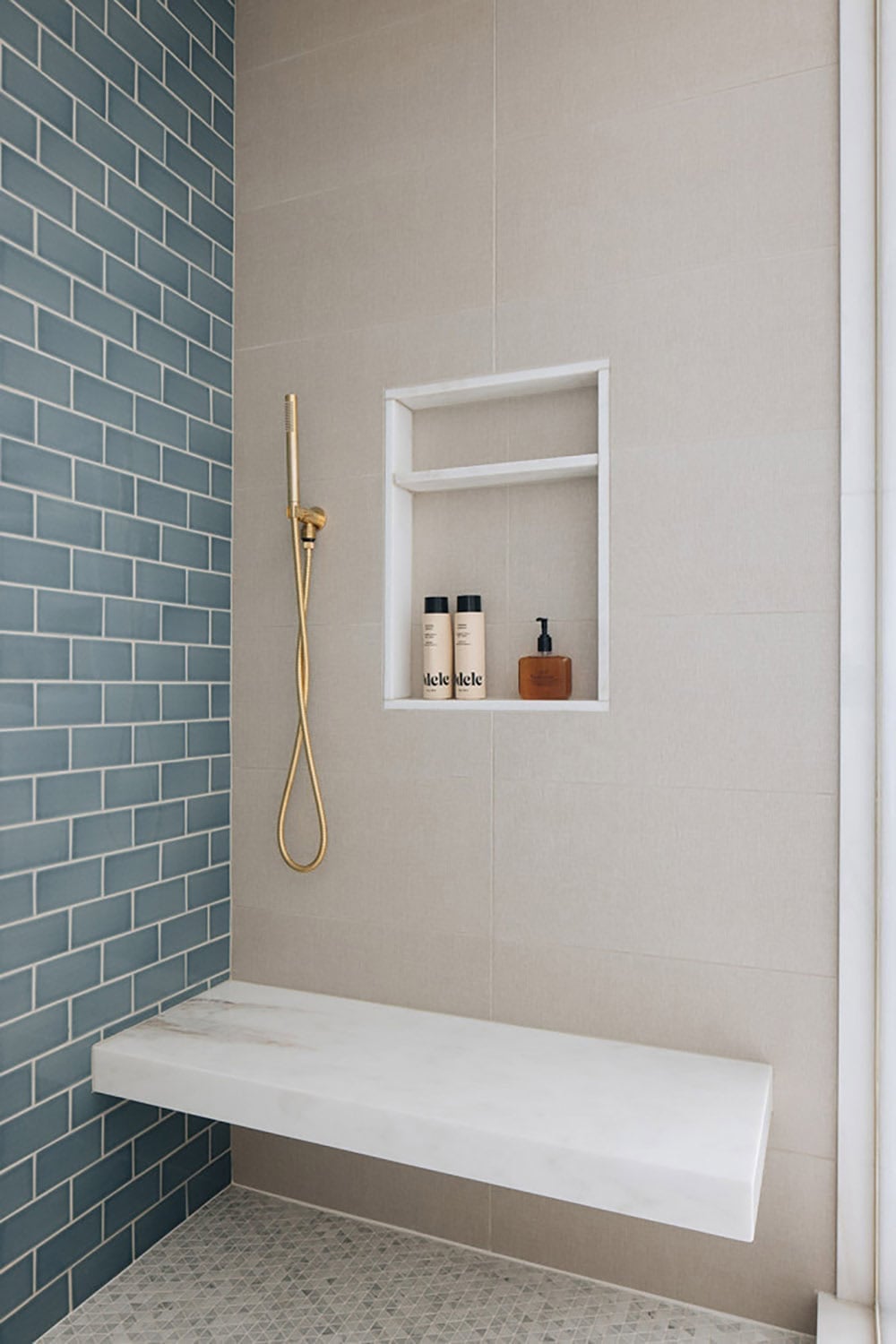Walk-in shower with blue subway tile, gold fixtures, and marble bench