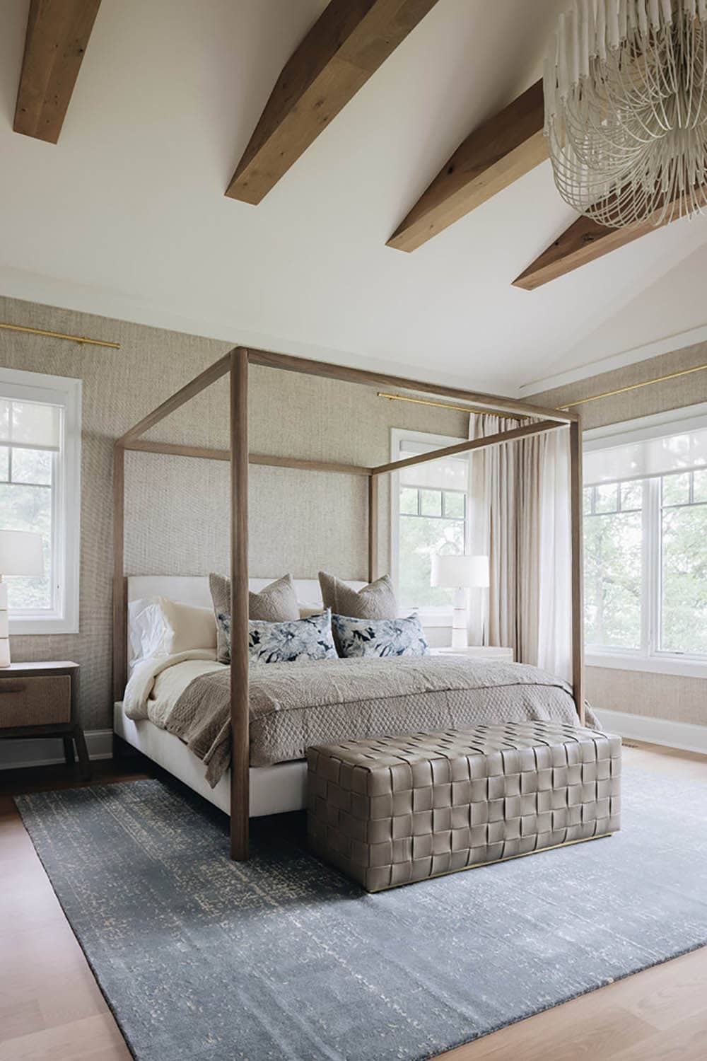 Primary bedroom with wood canopy bed, woven chandelier, and grasscloth walls